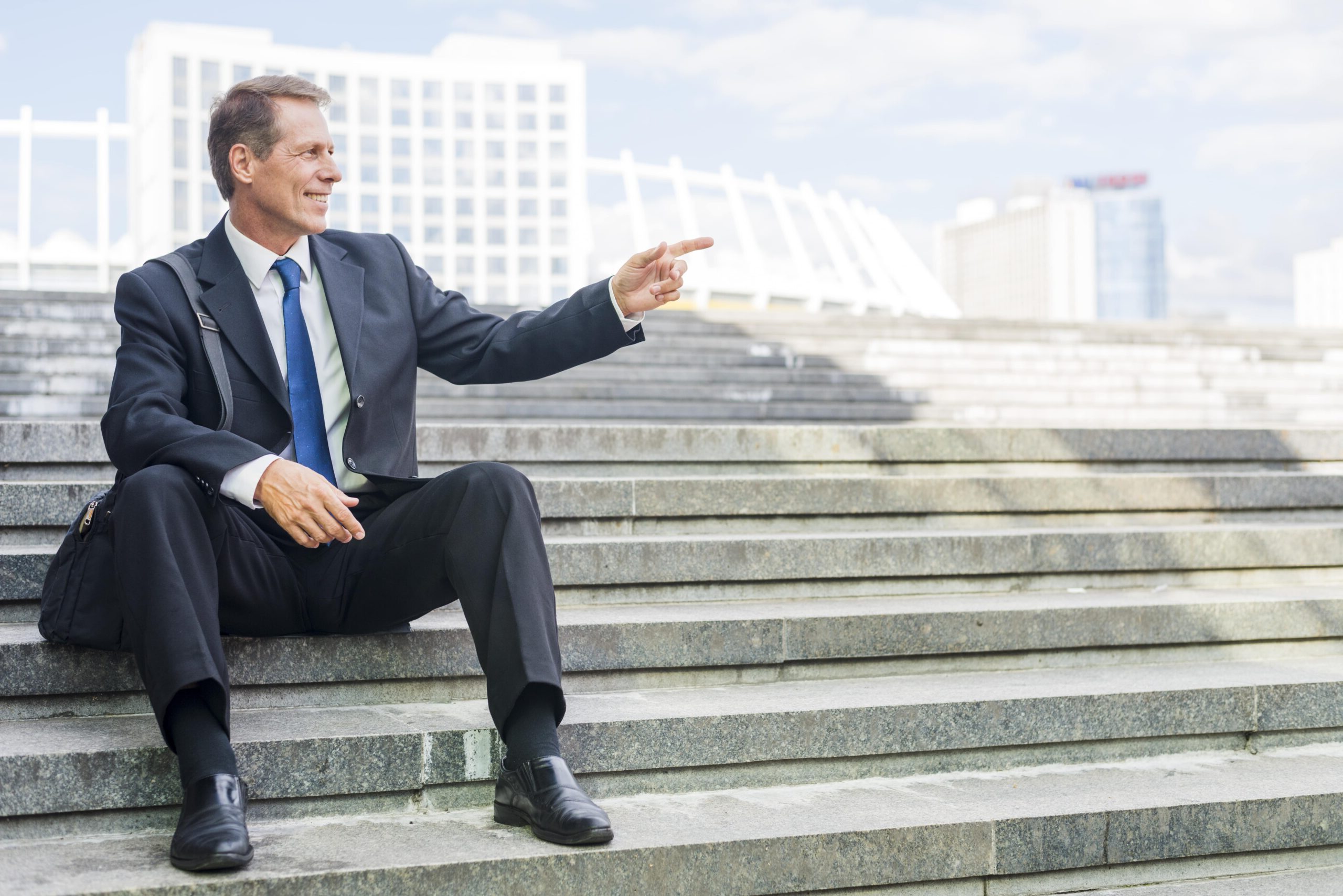 smiling-mature-businessman-pointing-something-while-sitting-staircase-min