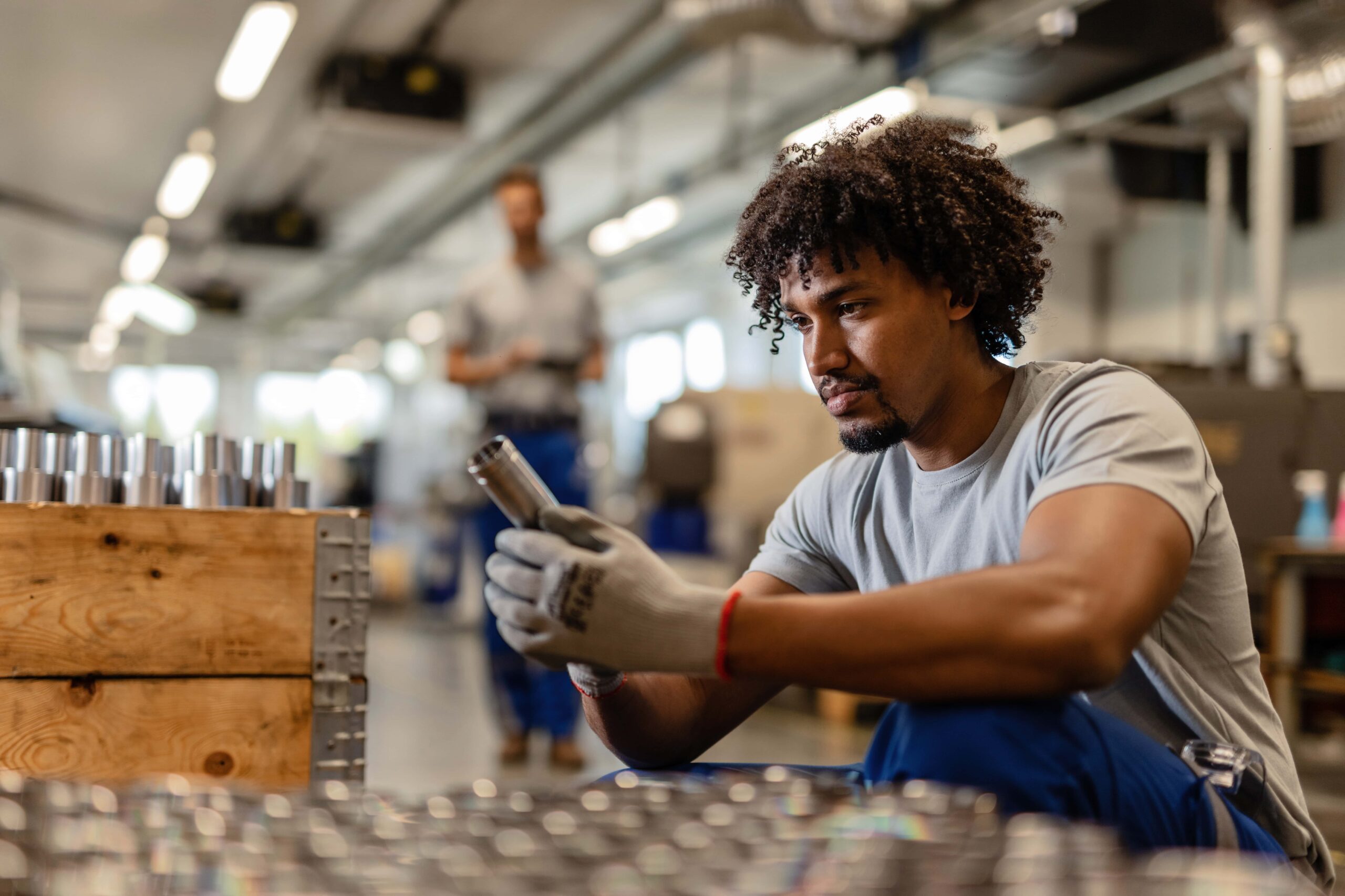 young-black-worker-examining-stainless-steel-cylinder-rod-while-working-distribution-warehouse-min